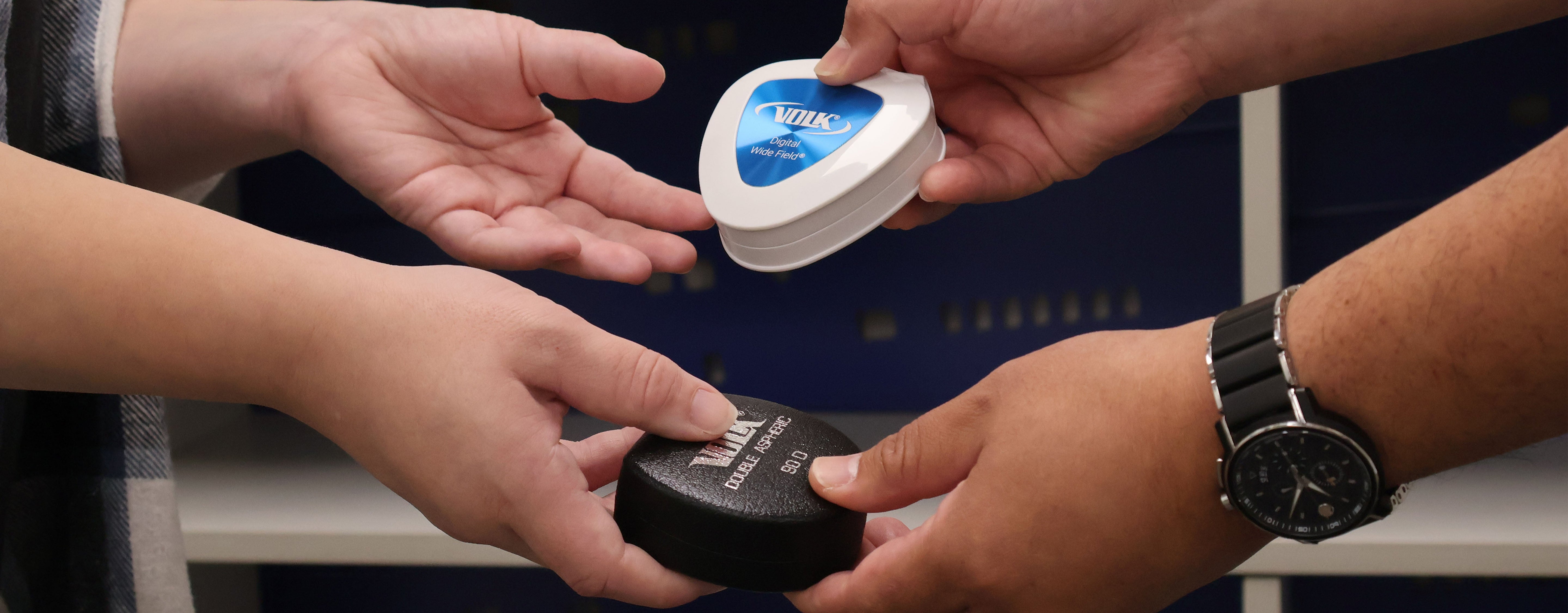 Two pairs of hands exchanging a clear plastic container with a blue lid, likely containing dental retainers.